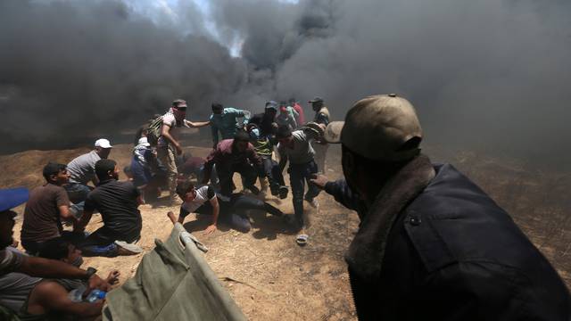 Wounded Palestinian demonstrator is evacuated as others take cover from Israeli fire and tear gas during a protest against U.S. embassy move to Jerusalem and ahead of the 70th anniversary of Nakba, at the Israel-Gaza border in the southern Gaza Strip