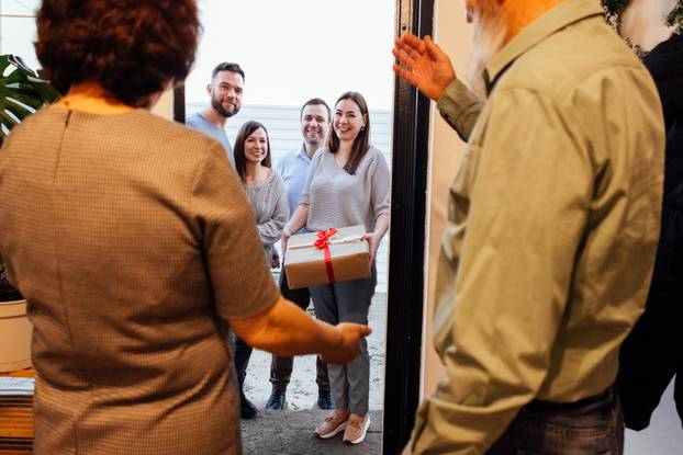 A mature couple greets their smiling guests at home