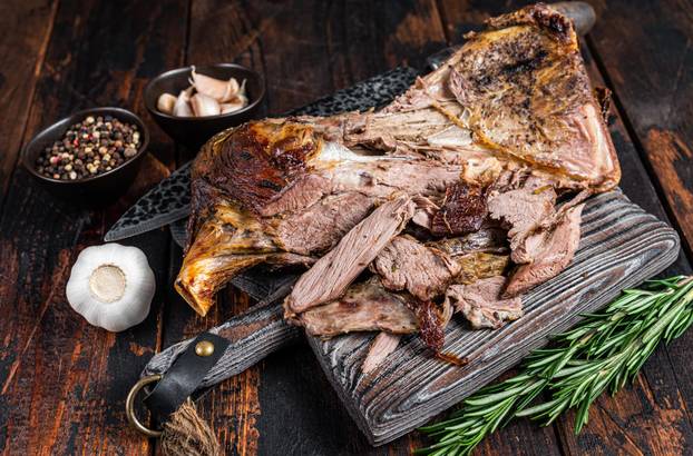 Baked lamb mutton cutting shoulder meat on a wooden board. Dark wooden background. Top view