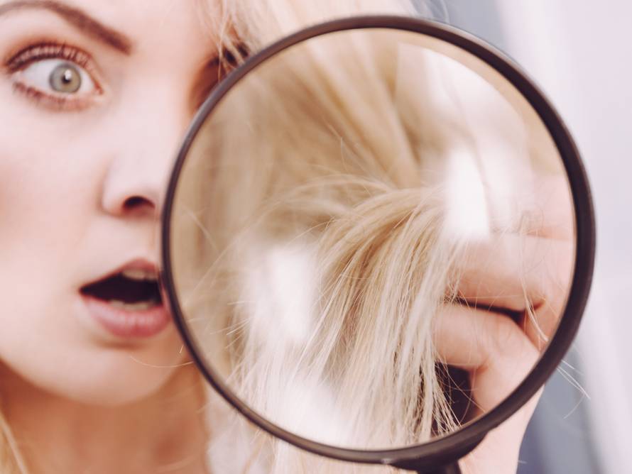 Woman looking at hair ends through magnifying glass