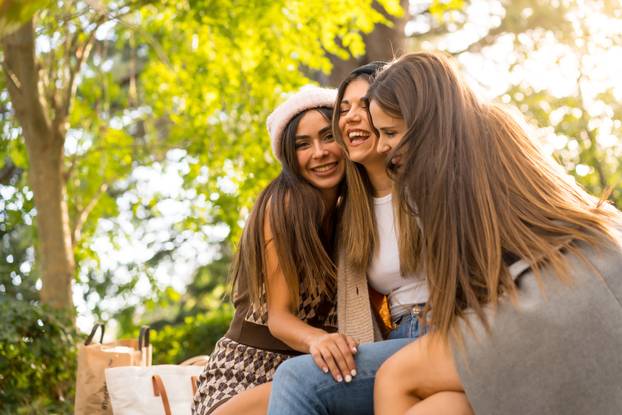 Women friends sitting hugging in a park in autumn at sunset, lifestyle and autumnal outfit