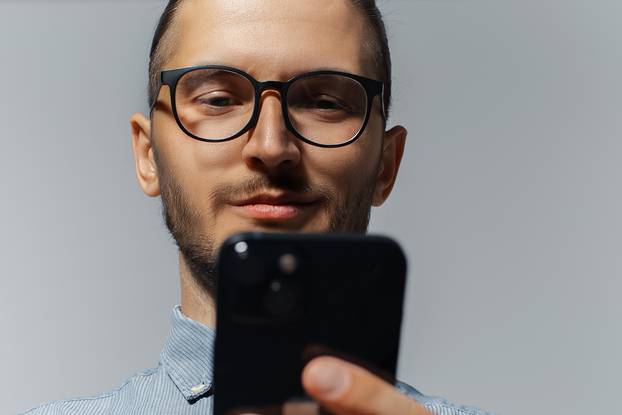 Close-up studio portrait of smiling guy looking in smartphone, w