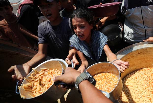 Palestinians wait to receive food cooked by a charity kitchen, in Gaza City