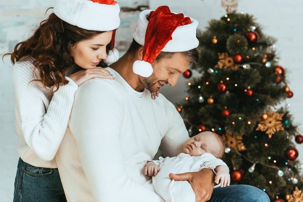 happy woman looking at sleeping baby over shoulder of husband