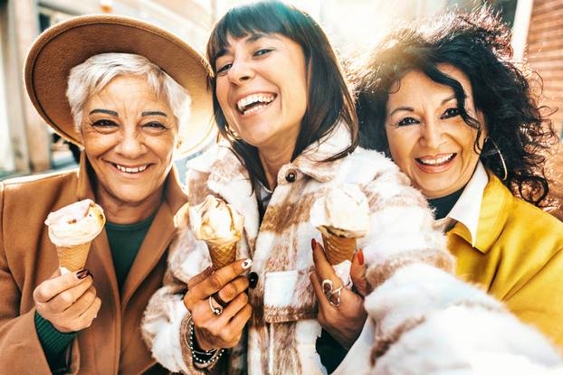Three mature women eating ice cream cone outside