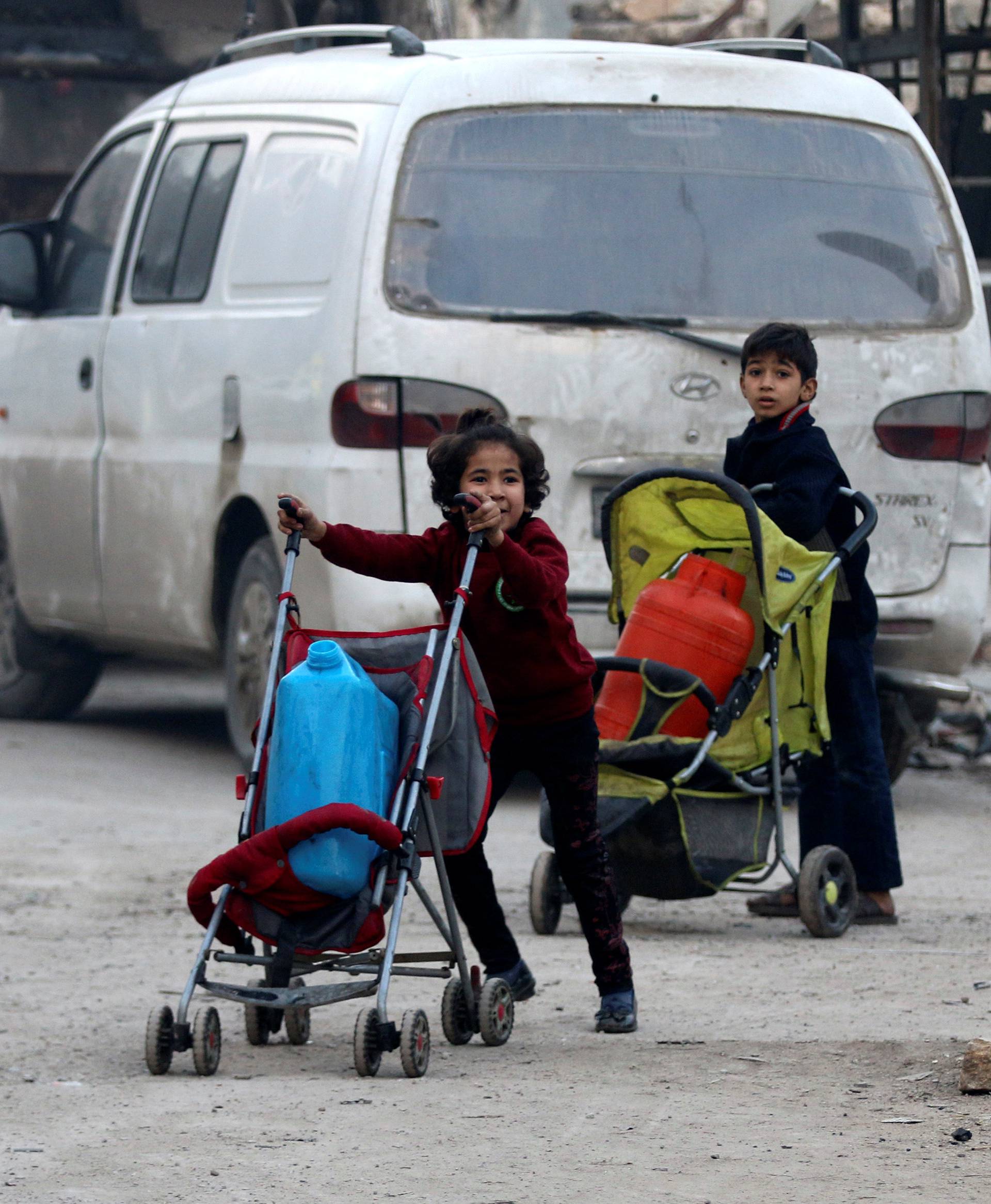Children push containers in strollers as they flee deeper into the remaining rebel-held areas of Aleppo