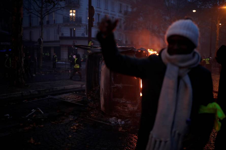 A protester wearing yellow vest, a symbol of a French drivers' protest against higher diesel taxes, stand near a burning car during clashes in a street near the Place de l'Etoile in Paris