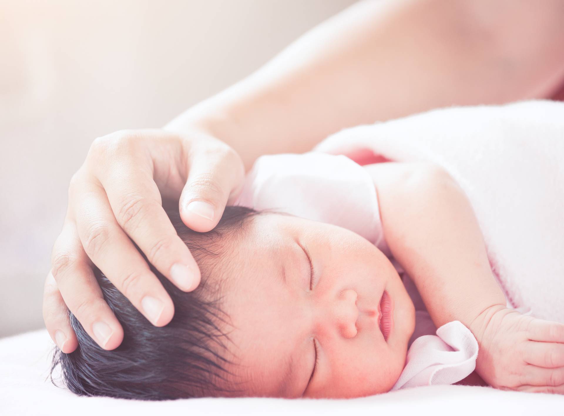 Mother hand touching asian newborn baby girl head while she slee