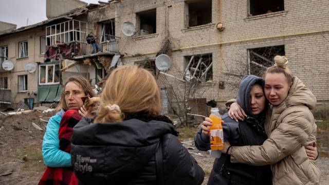 Locals react as they stand at the impact crater of a Russian S-300 missile that hit next to an apartment building in Peresichne