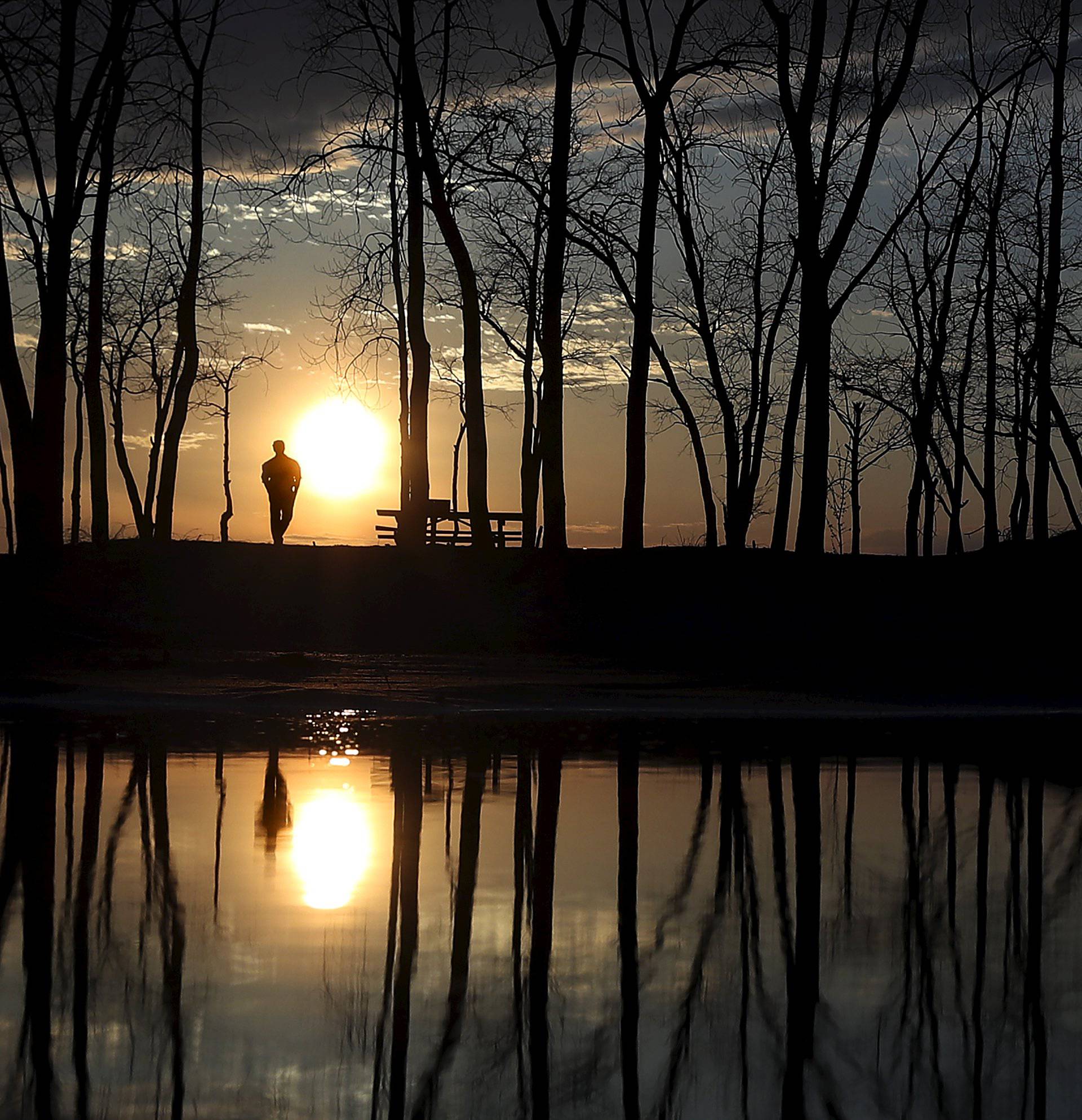 People stand and watch the sun set as they are reflected in a puddle at Presque Isle State Park in Erie, Pennsylvania