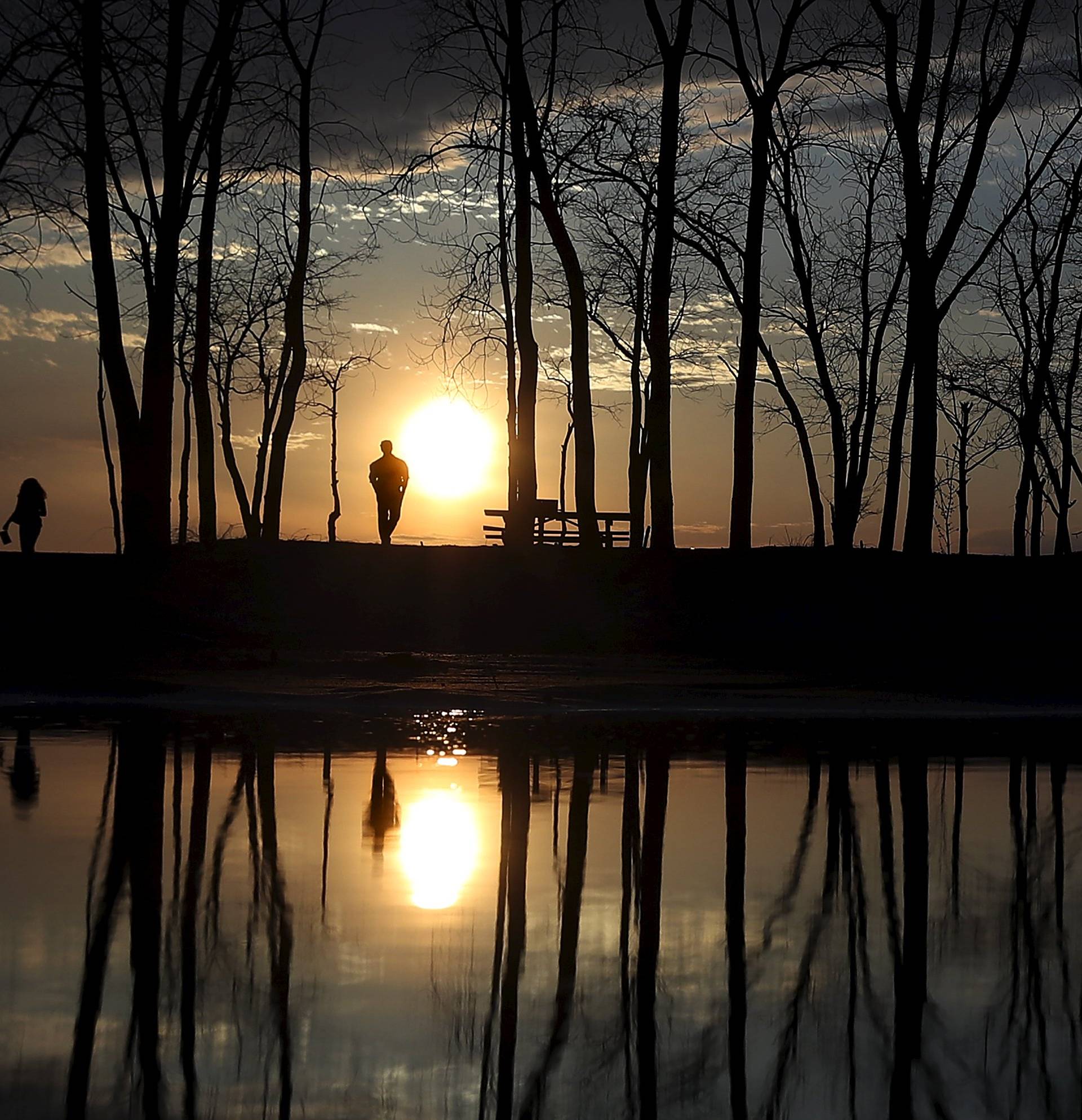 People stand and watch the sun set as they are reflected in a puddle at Presque Isle State Park in Erie, Pennsylvania