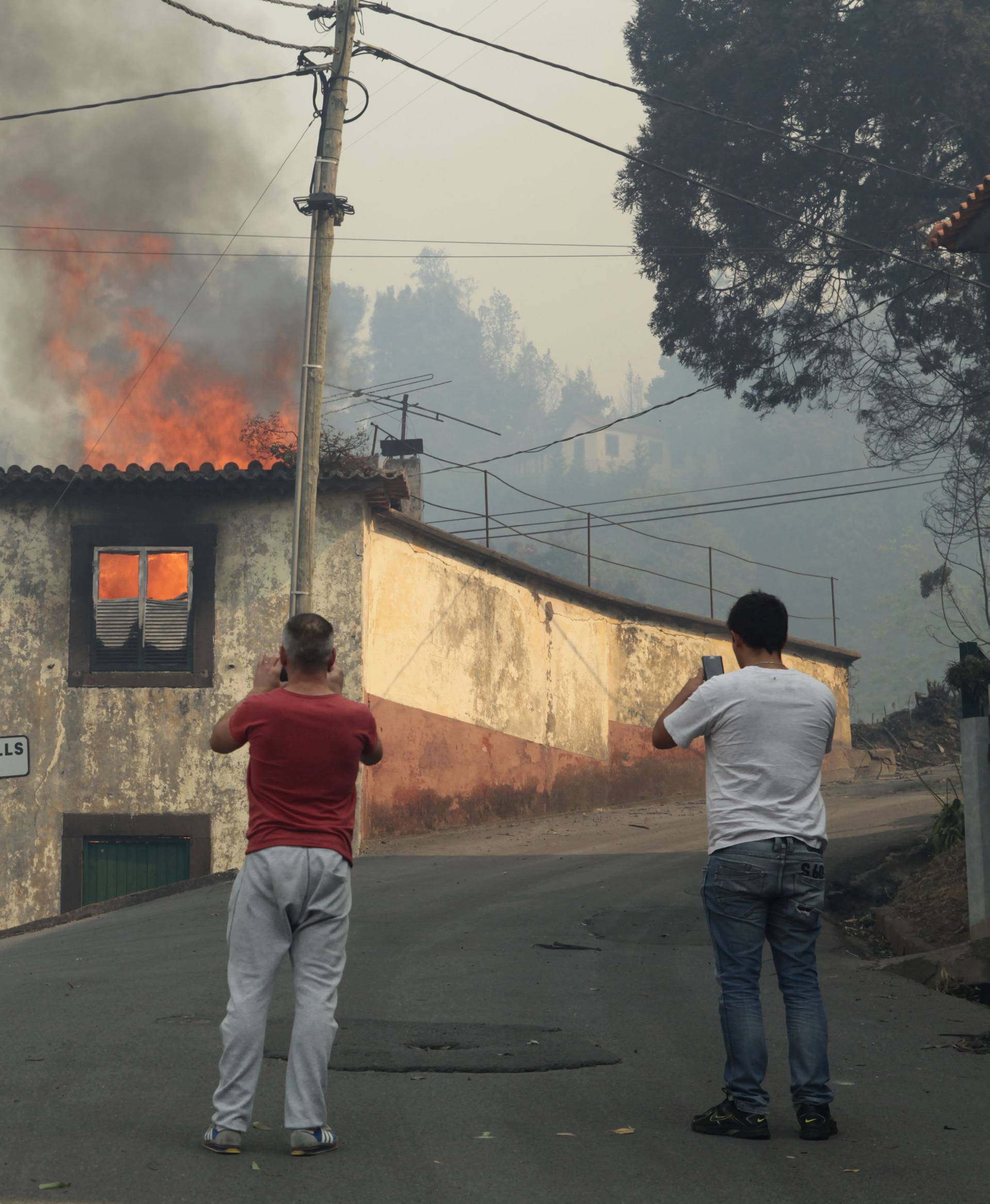 Men take pictures of a burning house at Caminho do Meio during the forest fires in Funchal