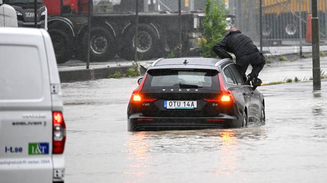 Man climbs out of a car that tried to get through a flooded roundabout in Arlov