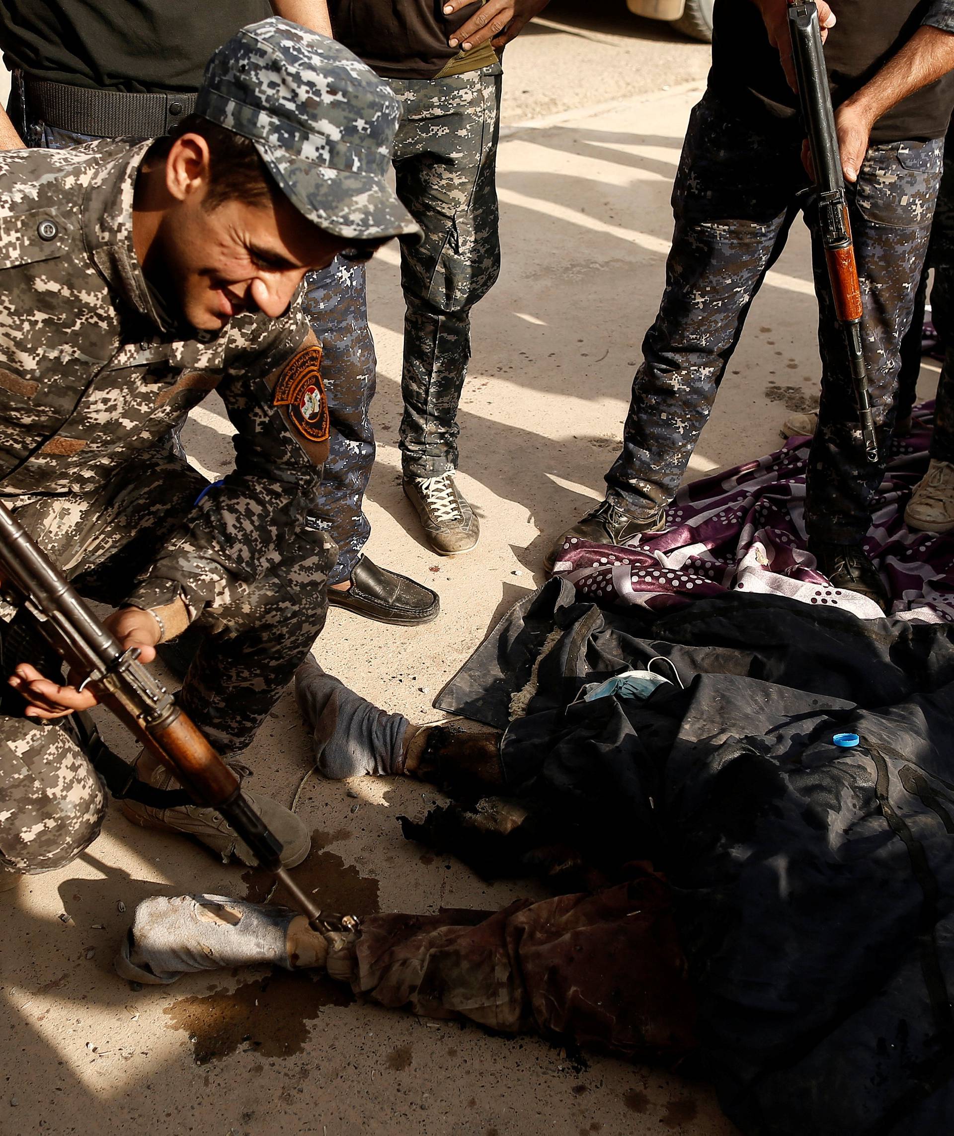 An Iraqi soldier smiles as he points his rifle towards the foot of a dead Islamic State fighter's body along a street of the town of al-Shura