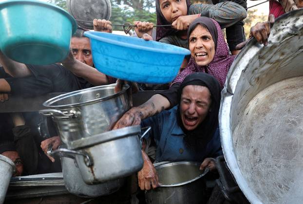 FILE PHOTO: Palestinians wait to receive food from a charity kitchen, amid a hunger crisis, in Gaza City