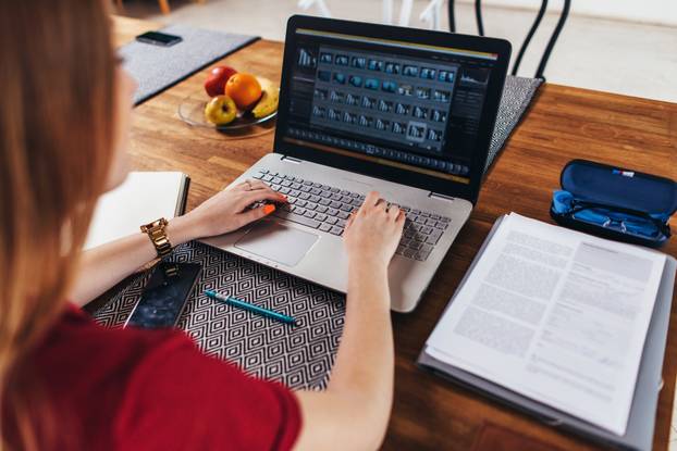 Woman working at home using laptop sitting at table in kitchen