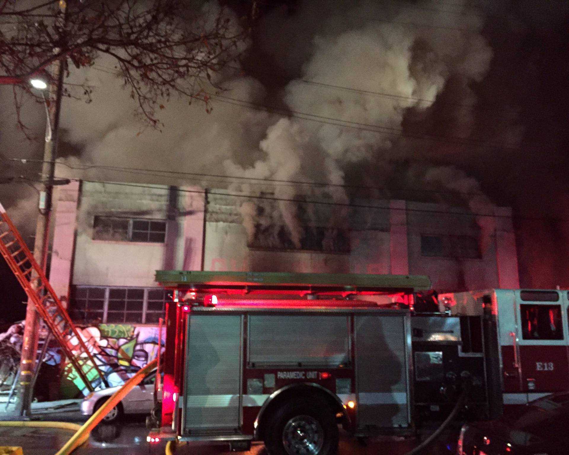 Smoke pours from a warehouse, which caught fire during a dance party in Oakland