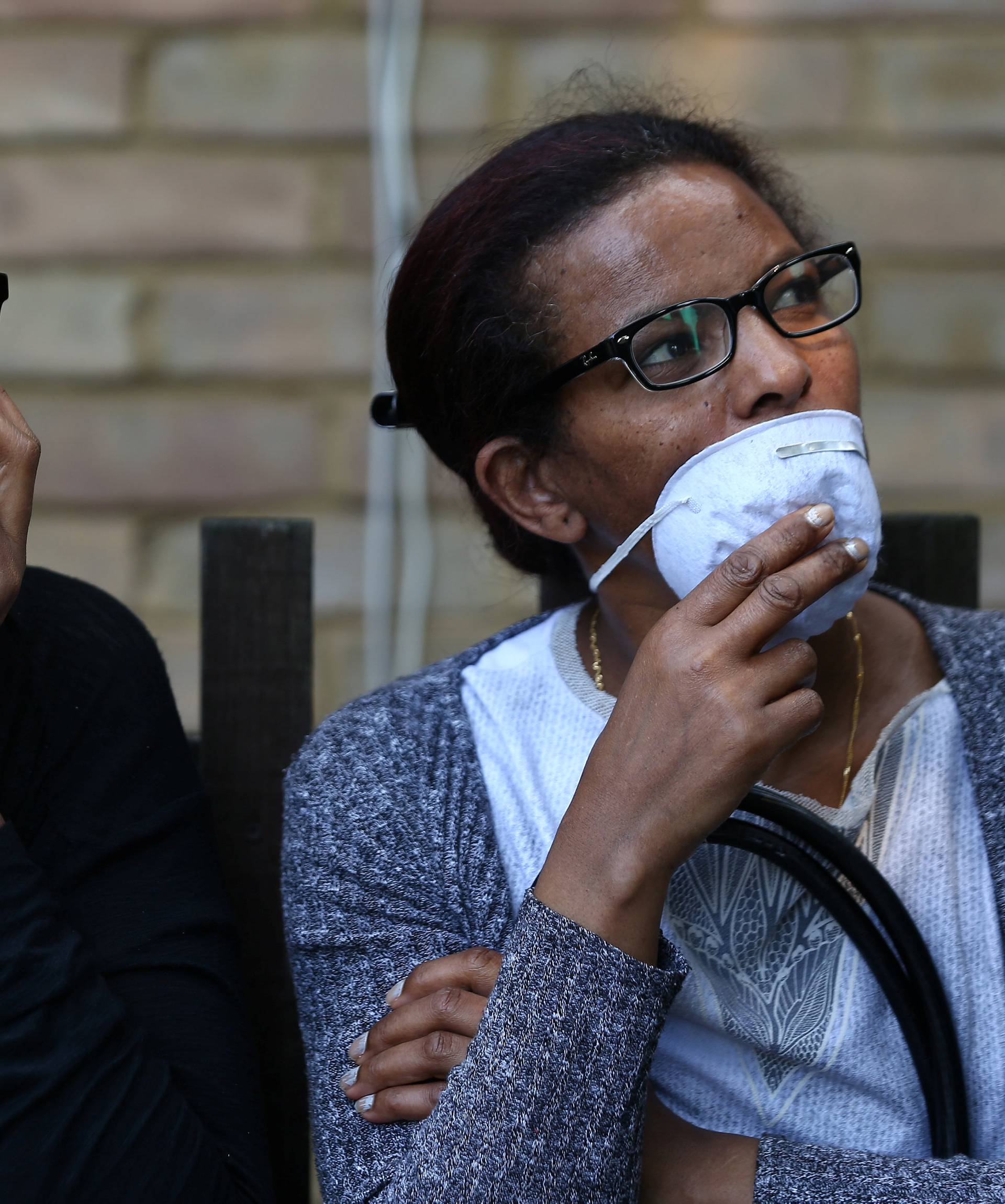 People wear masks near a tower block severely damaged by a serious fire, in north Kensington, West London