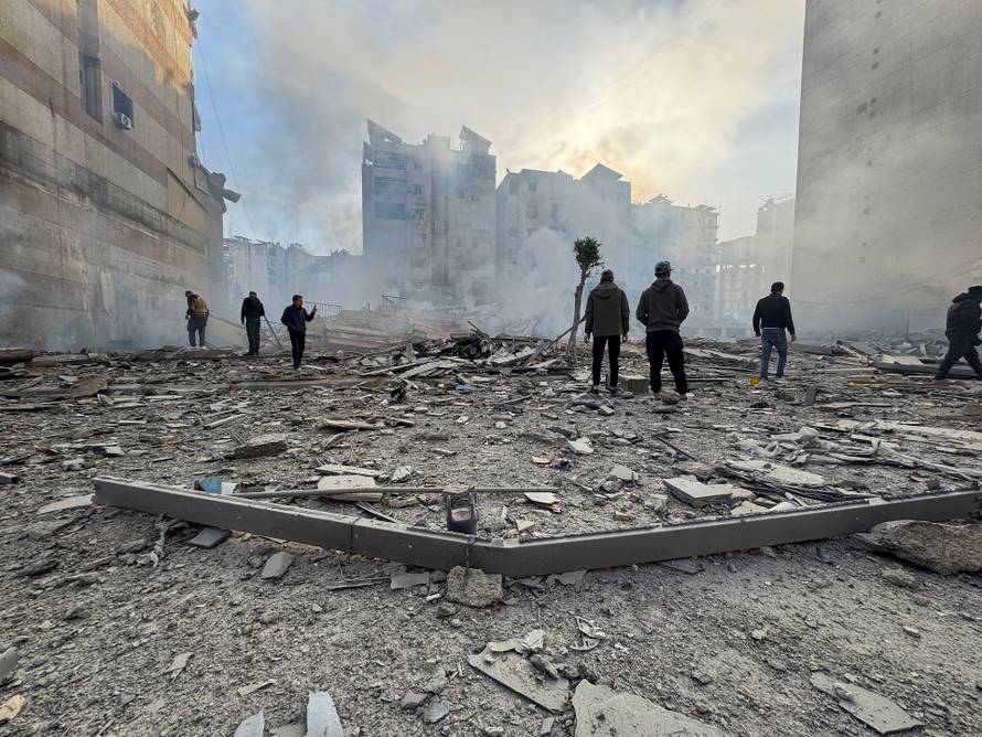 People stand on the rubble of a damaged building after an Israeli strike on Beirut's southern suburbs