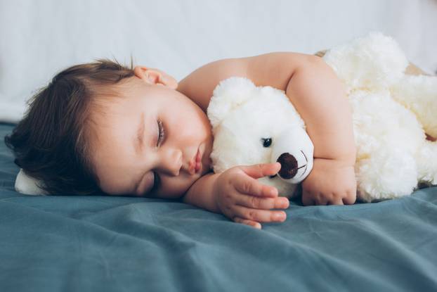 Beautiful baby sleeping with his teddy bear aside, family concep