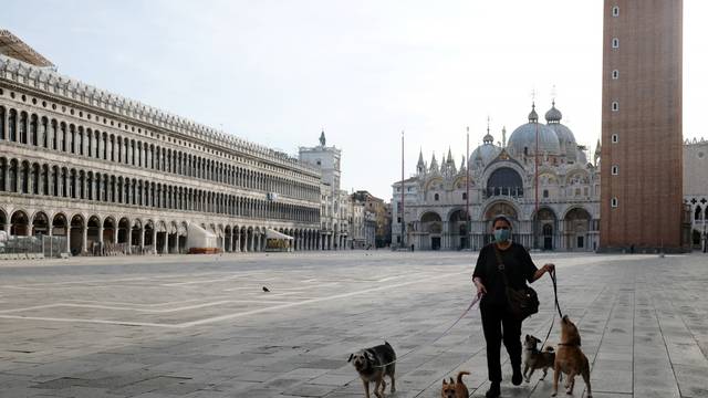 A woman walks with her dogs in St Mark's Square as Italy eases some of the lockdown measures put in place during the coronavirus disease (COVID-19) outbreak in Venice