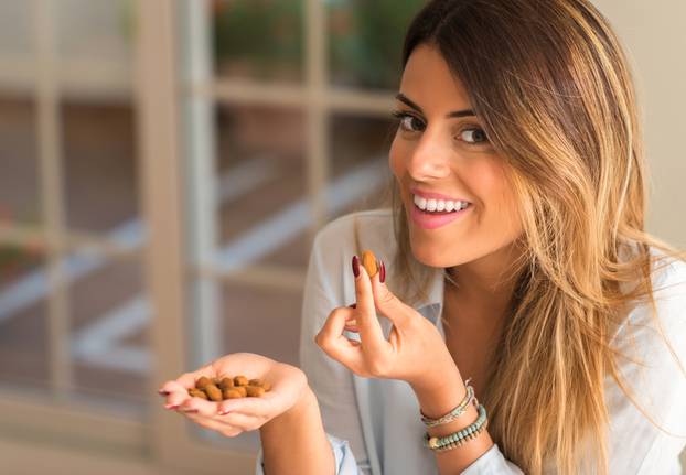 Beautiful,Young,Woman,Smiling,And,Eating,Nuts,At,Home.,Healthy