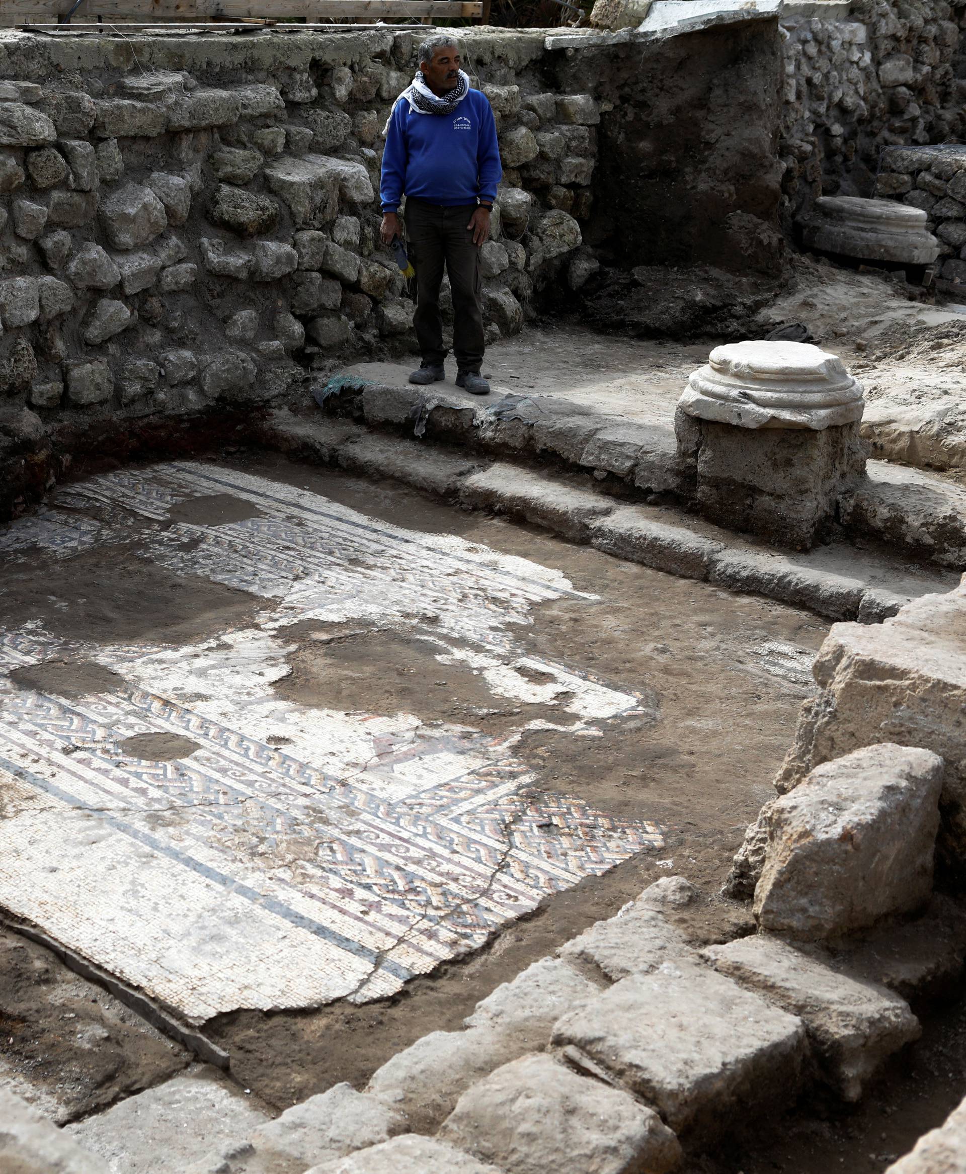 An Israel Antiquities Authority worker stands next to a mosaic floor which archaeologists say is 1,800 years old and was unearthed during an excavation in Caesarea