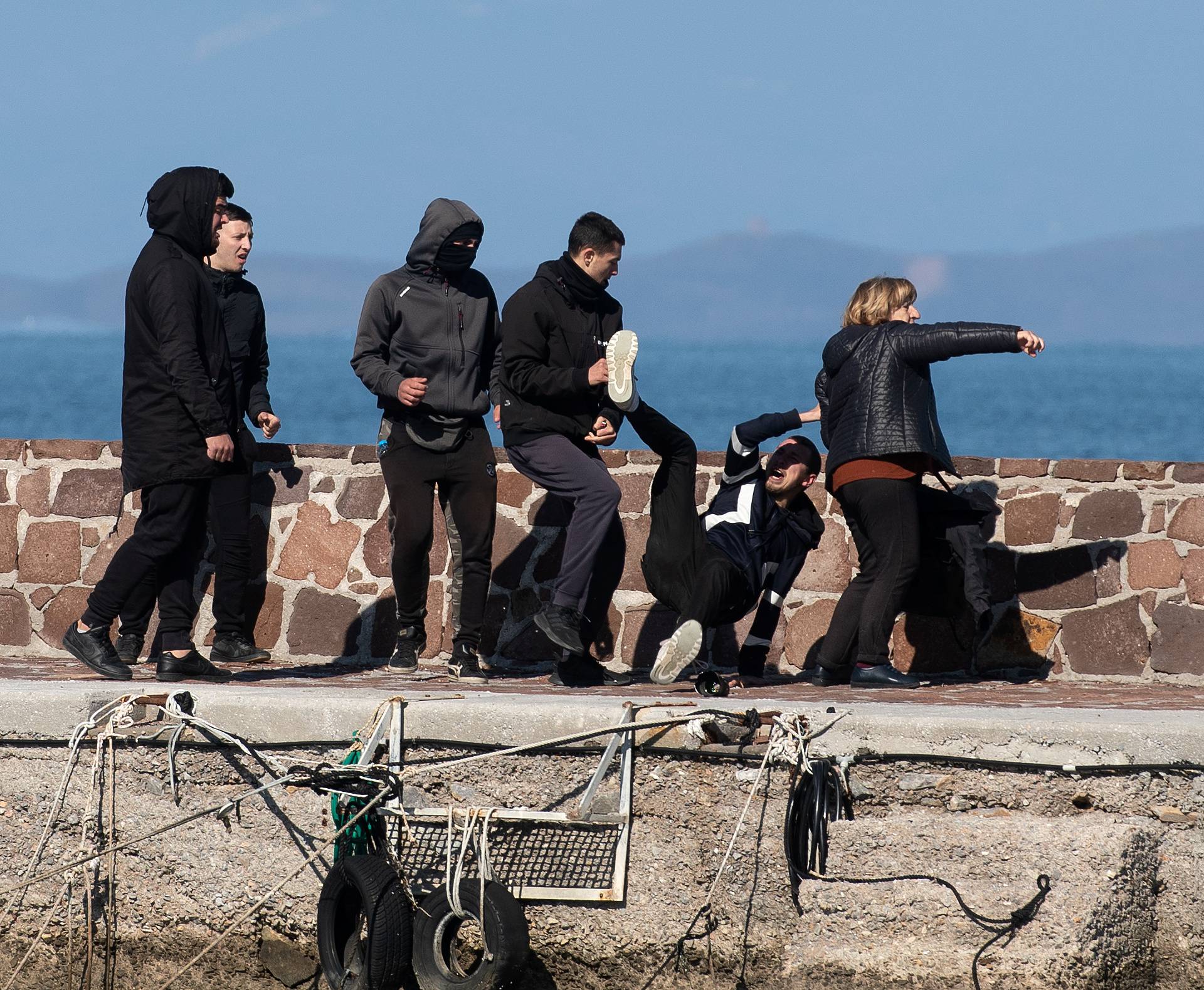 Locals who prevent migrants on a dinghy from disembarking at the port of Thermi beat a journalist, as a woman tries to stop them, on the island of Lesbos, Greece