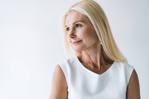 smiling blonde elegant mature woman looking away isolated on grey