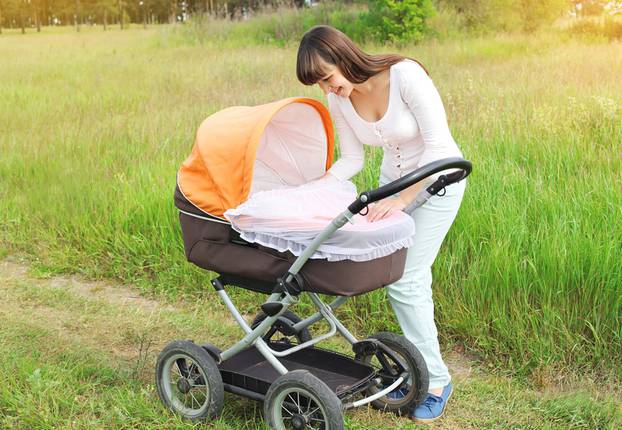 Happy young smiling mother walking with baby stroller outdoors o