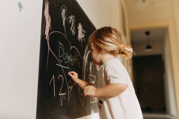 A little girl drawing on a chalkboard with chalk.
