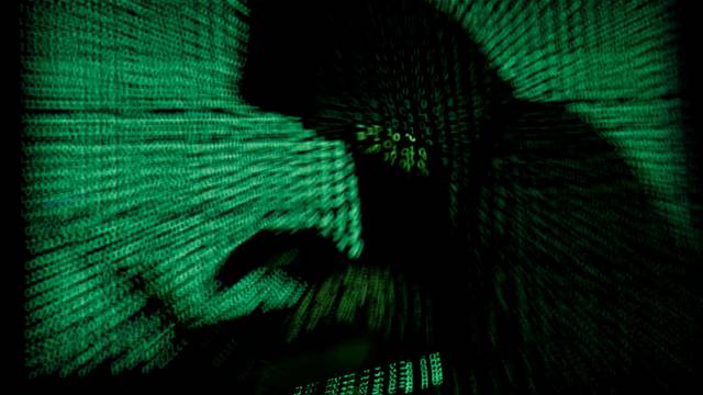 FILE PHOTO: Hooded an holds laptop computer as cyber code is projected on him in this illustration picture