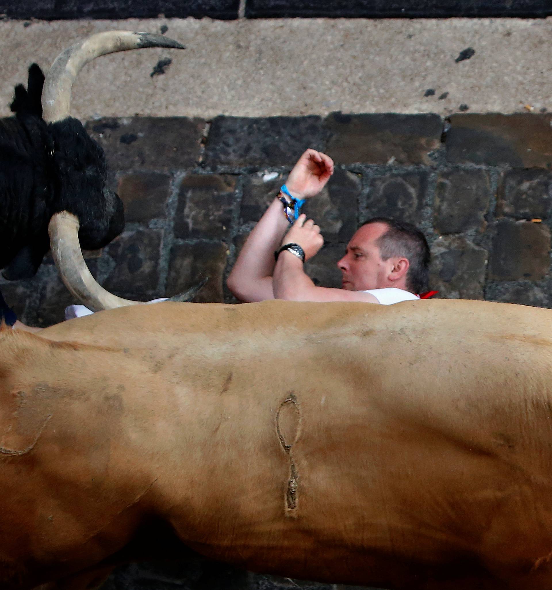 A runner falls under Cebada Gago bulls during the first running of the bulls at the San Fermin festival in Pamplona