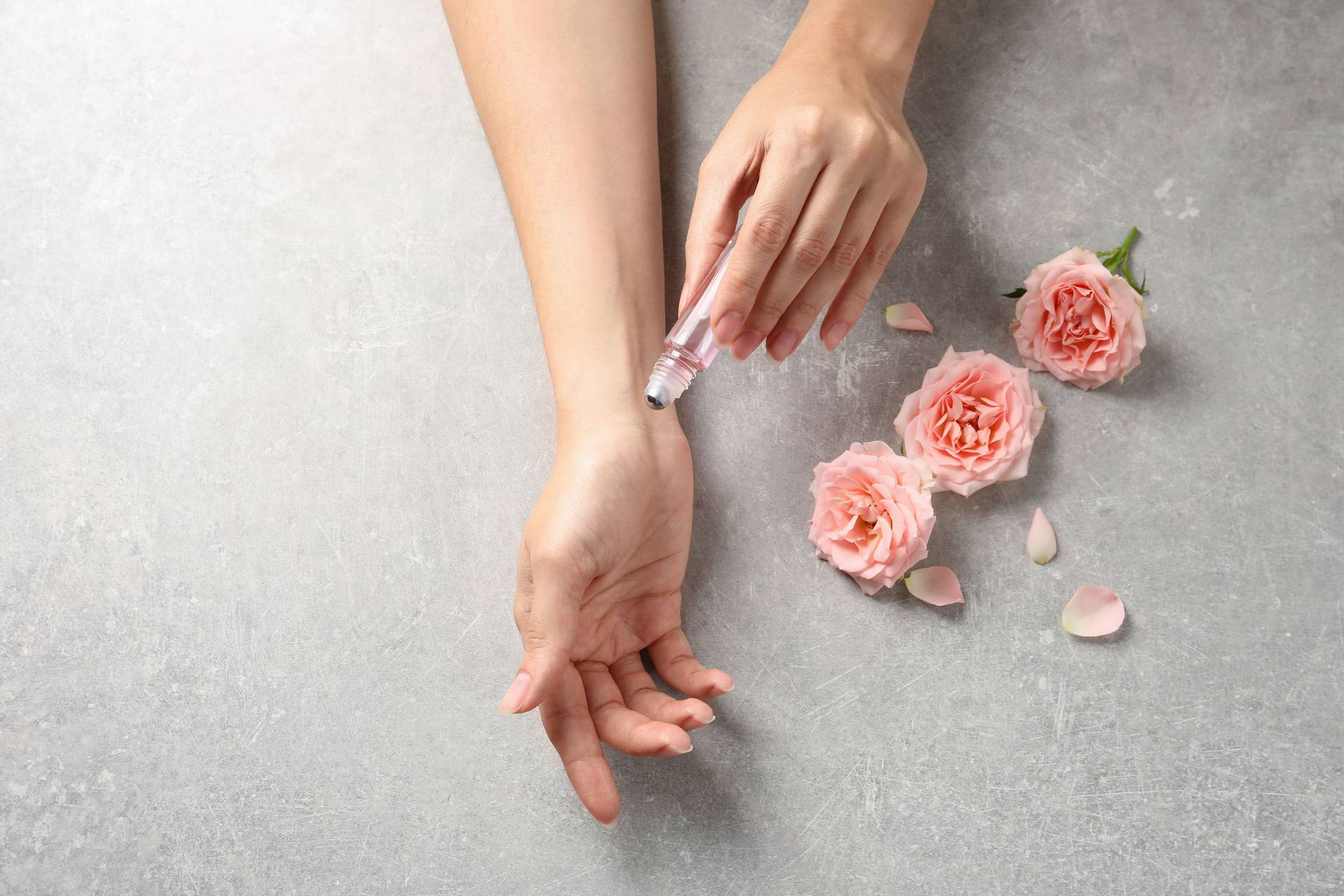 Woman applying rose essential oil on wrist and flowers at grey t