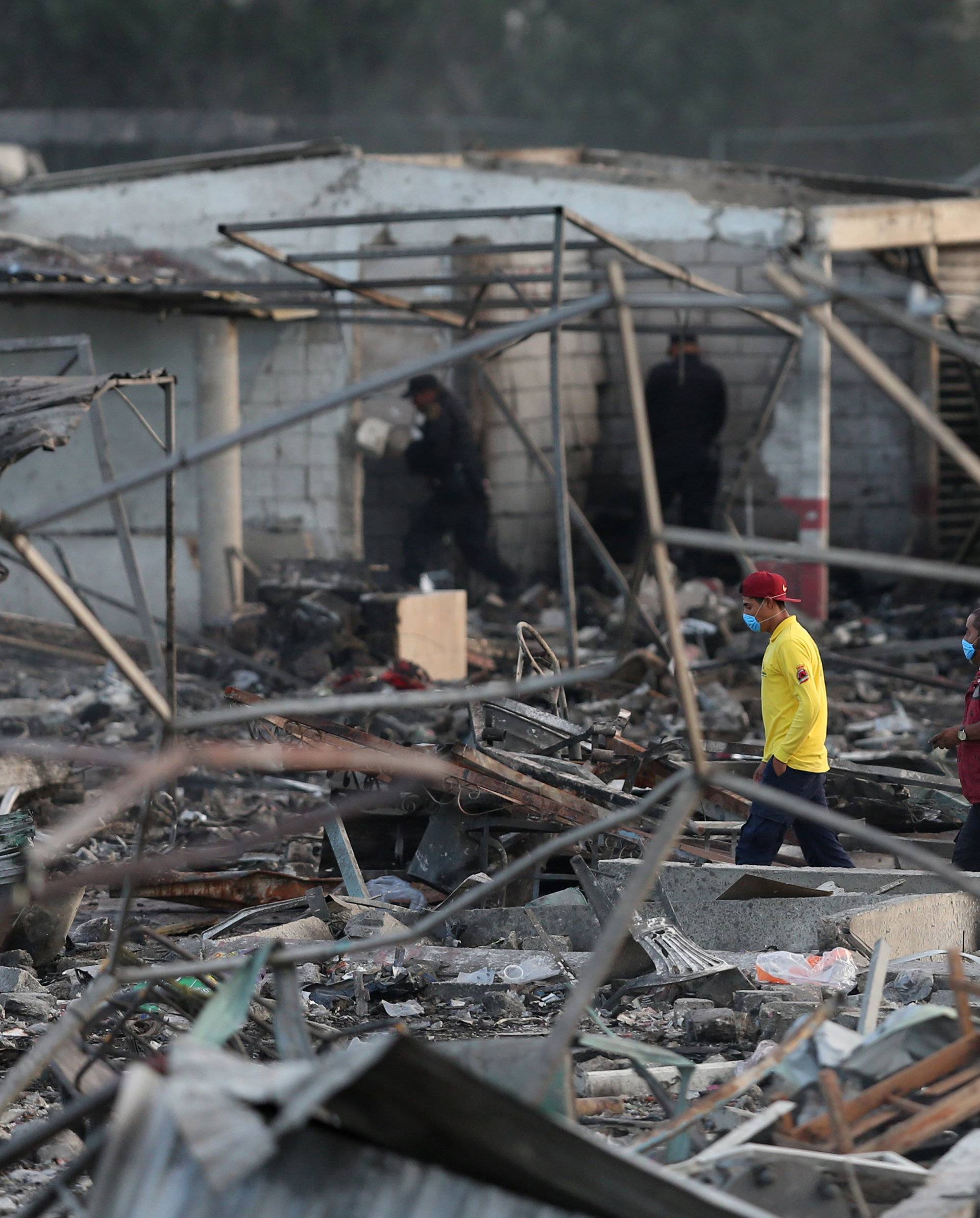 People walk amidst the remains of houses destroyed in an explosion at the San Pablito fireworks market in Tultepec