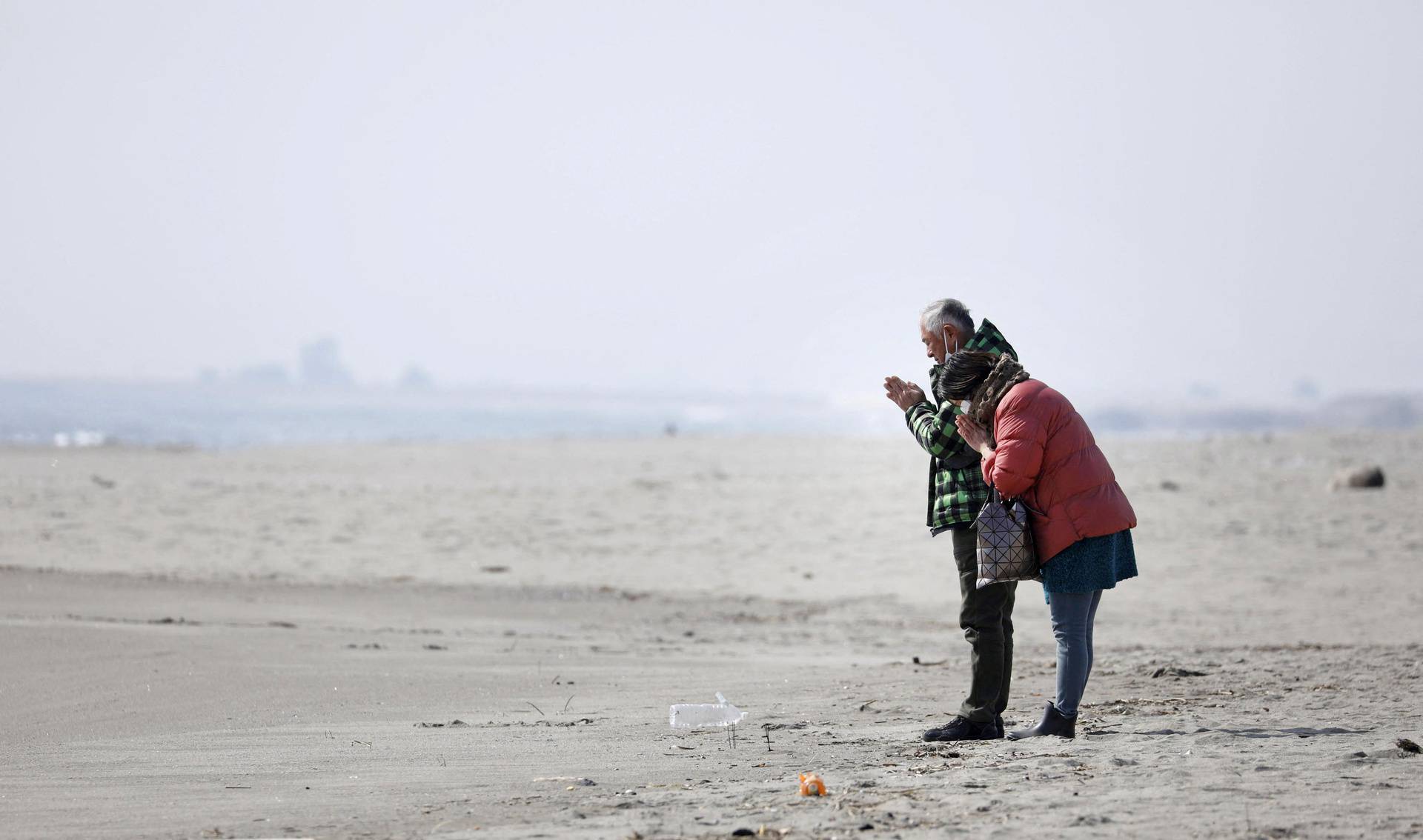 A couple prays on a beach in the Arahama district of Sendai