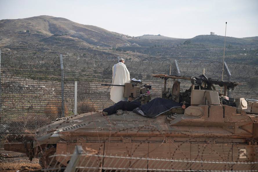 Israeli soldiers on a Namer Armoured Personnel Carrier (APC) while one of them conducts morning prayers, along the Golan Heights side of the ceasefire line between Syria and the Israeli-occupied Golan Heights