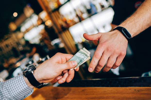 Close up of two hands. The customer's hand is giving some cash to a barman's hand for the drink. Cut view.