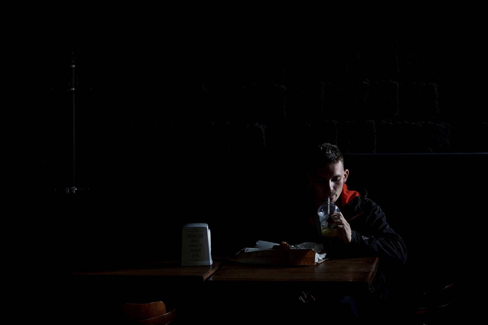 Local resident drinks a lemonade inside a dark cafe during an electricity power cut due to a Russian missile attack, in Mykolaiv