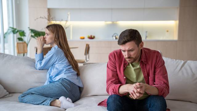 Couple man woman ignoring each other sitting on couch in silence at home turning away.