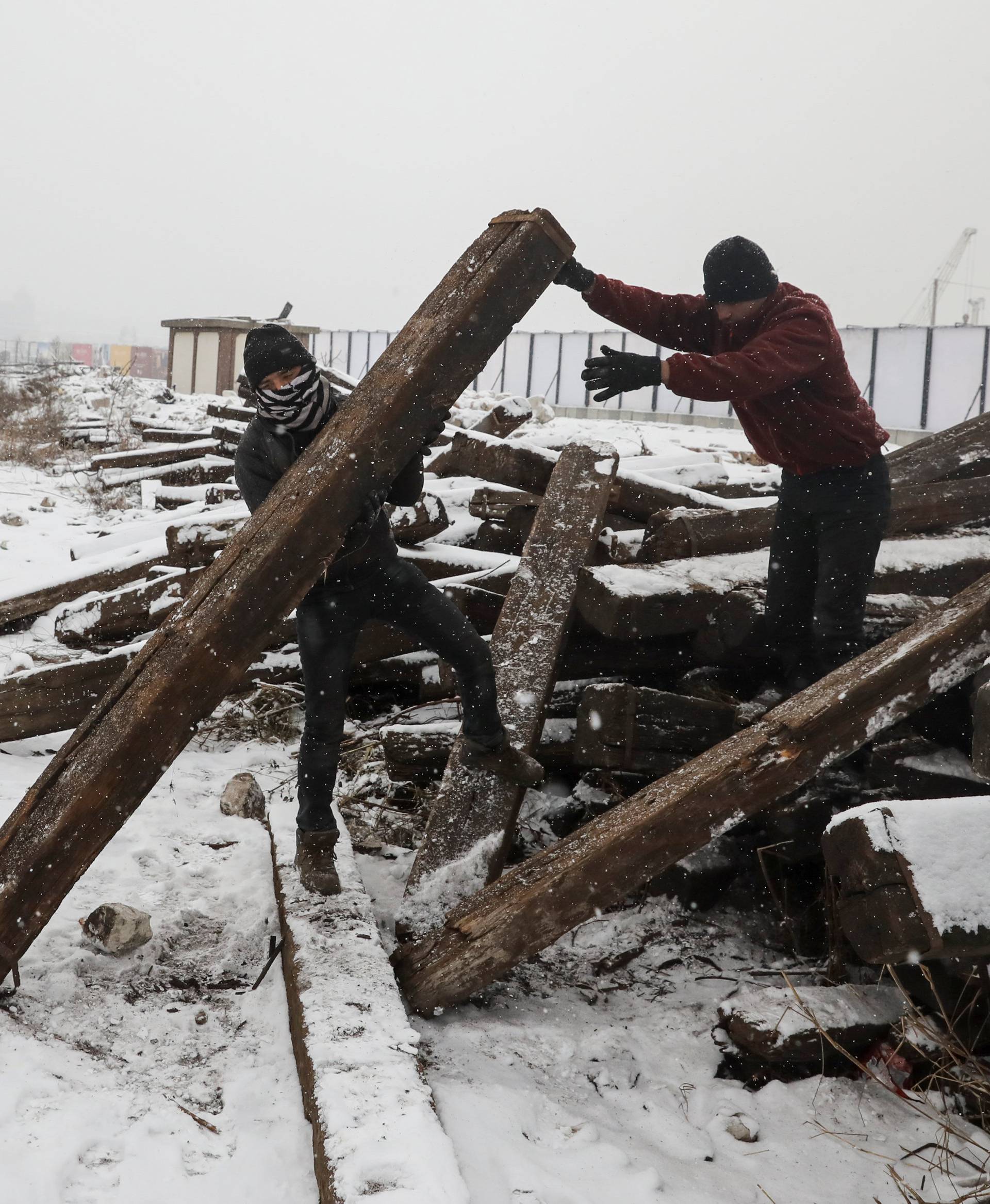 Migrants take away a railway sleeper during a snowfall outside a derelict customs warehouse in Belgrade