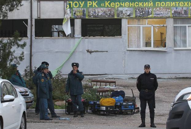 A Russian policeman and Emergencies Ministry members gather outside the damaged building of a college following a recent attack in Kerch