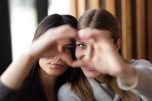 Two lovely girls smiling in a cafe and making a hearth shape wit