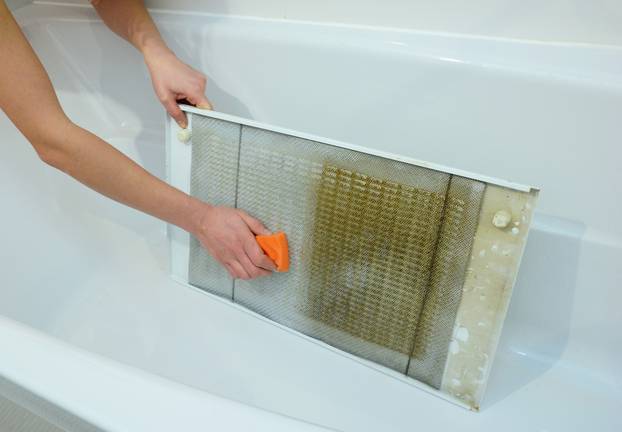 Woman cleaning kitchen hood filter in bath tub with sponge