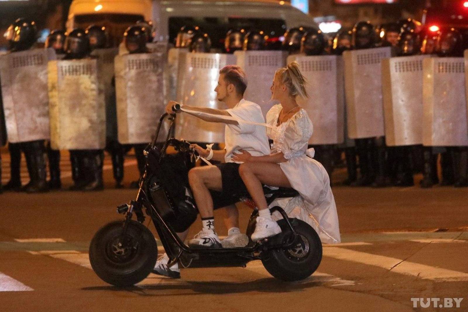 A couple rides on a scooter in front of law enforcement officers blocking a street after poll closed at presidential election in Minsk