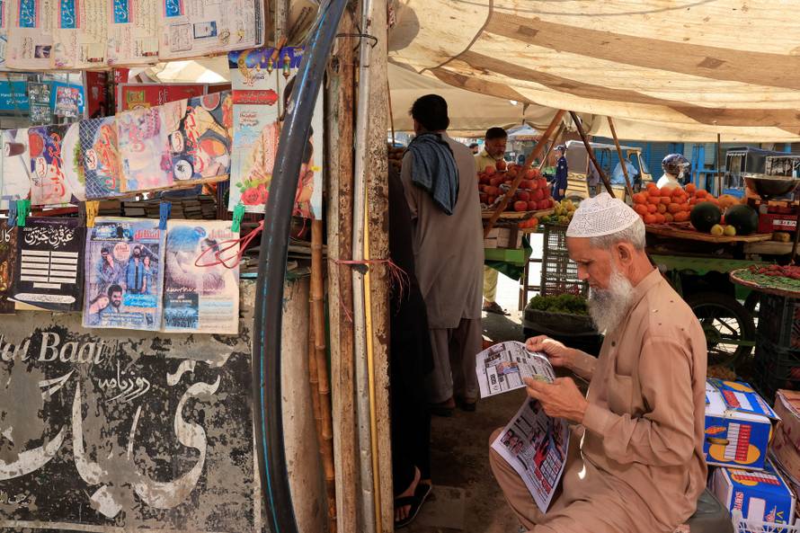 A man reads a newspaper, following the news of exchanges of fire between Pakistan and Afghanistan forces, at a stall along a market in Karach