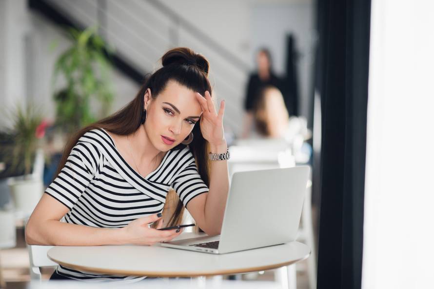 Bad news. Depressed young woman with long brunette hair looking at mobile phone while sitting indoors.