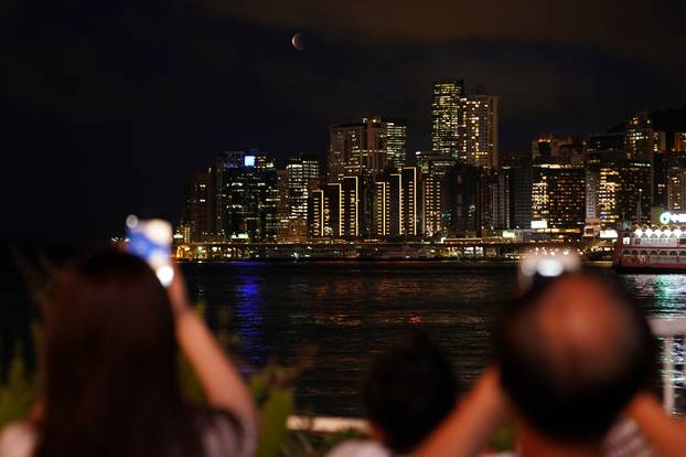 People take pictures during the full moon eclipse, known as the "Super Blood Moon", rises through low clouds above the Eastern District of Hong Kong