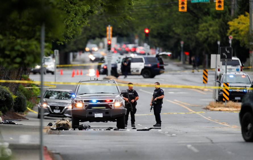 Police officers gather after two armed men entering a bank were killed in a shootout with the police in Saanich