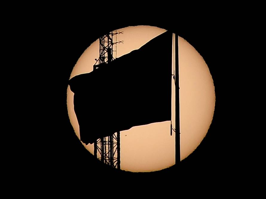 An American flag is silhouetted as the planet Mercury is seen, lower left quadrant, transiting across the face of the sun in Las Vegas